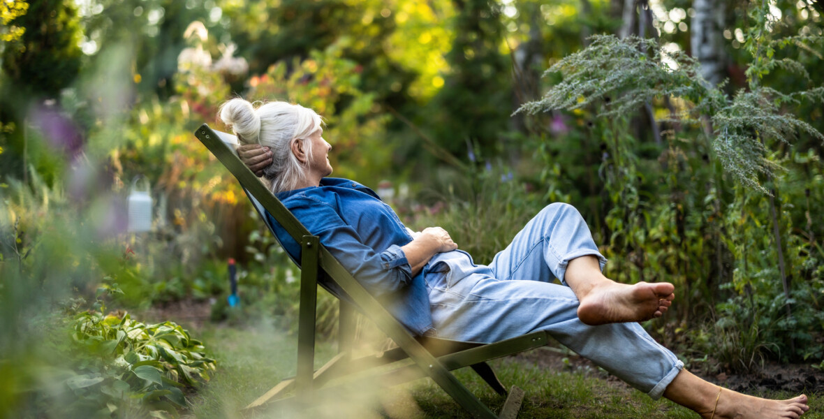 Kvinna sitter i en solstol i trädgård