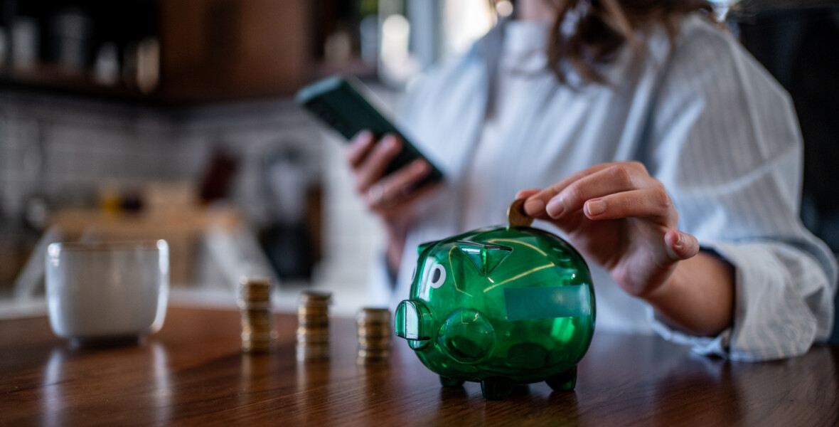 Kvinna lägger mynt i grön spargris