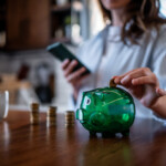 Kvinna lägger mynt i grön spargris