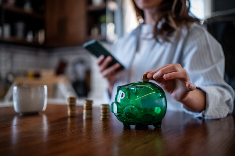 Kvinna lägger mynt i grön spargris