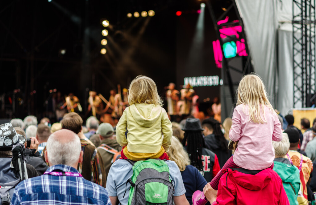 Barn sitter på vuxnas axlar under en konsert.