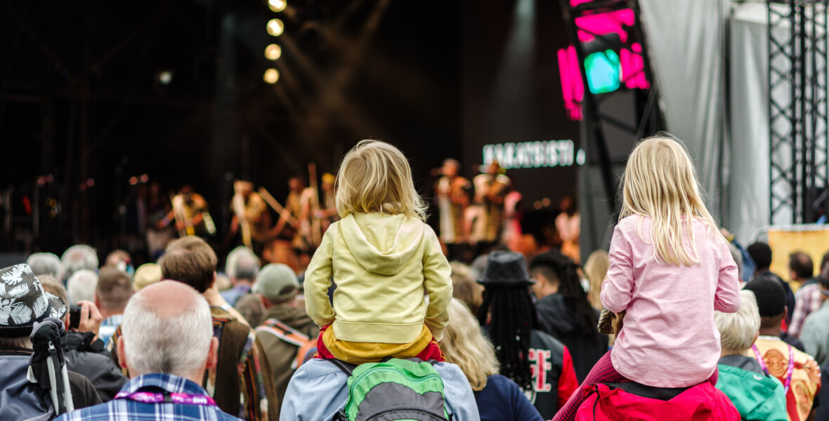 Barn sitter på vuxnas axlar under en konsert.