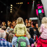 Barn sitter på vuxnas axlar under en konsert.